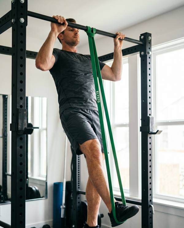 Man doing band-assisted pull-ups with a KLYSTO resistance band looped over a bar